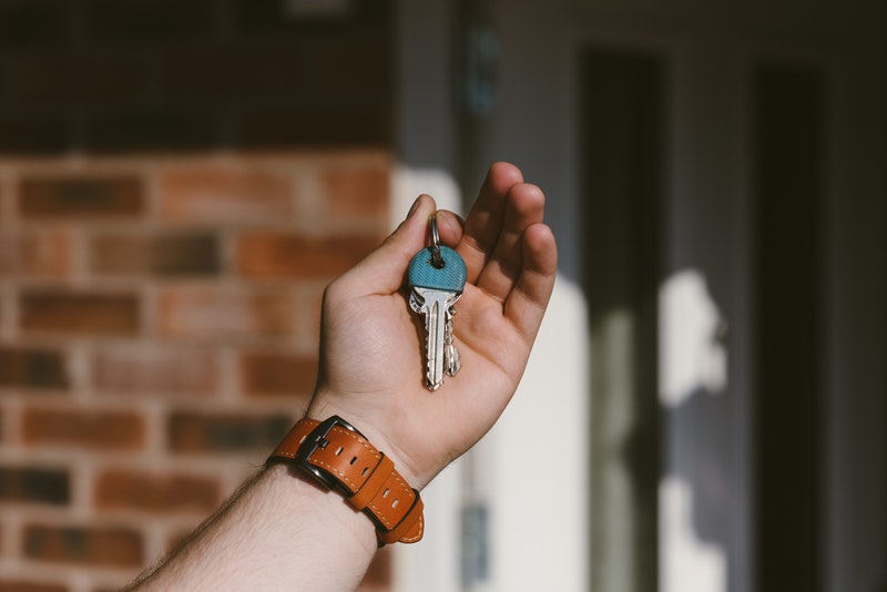 a hand holding house keys in front of a house